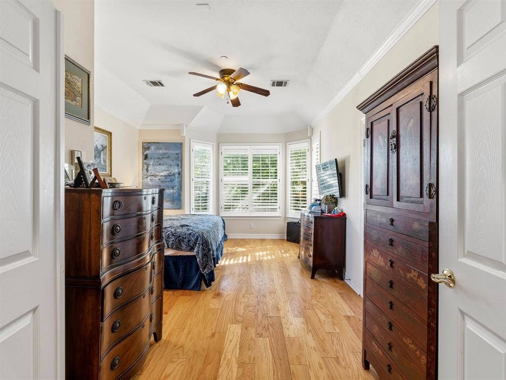 14567 Juliard Lane, Addison, TX 75001 Tray ceiling with a central multi-blade ceiling fan and wood-finish flooring, complemented by a bay window featuring white plantation shutters