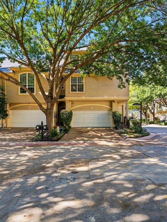 14567 Juliard Lane, Addison, TX 75001 Multi-level townhouse exterior featuring stucco siding, arched garage entries, divided-light windows, and a mature tree canopy