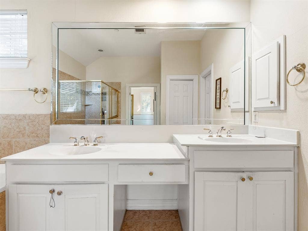 14567 Juliard Lane, Addison, TX 75001 Dual-sink vanity with white cabinetry, light-toned countertop, large-format mirror, and brushed-finish fixtures