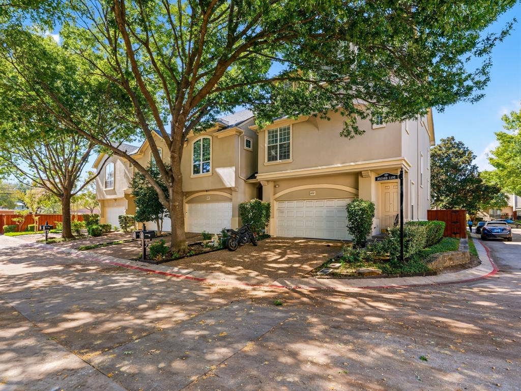 14567 Juliard Lane, Addison, TX 75001 Multi-story exterior featuring a neutral stucco facade, arched windows, attached multi-car garages, and mature shade trees