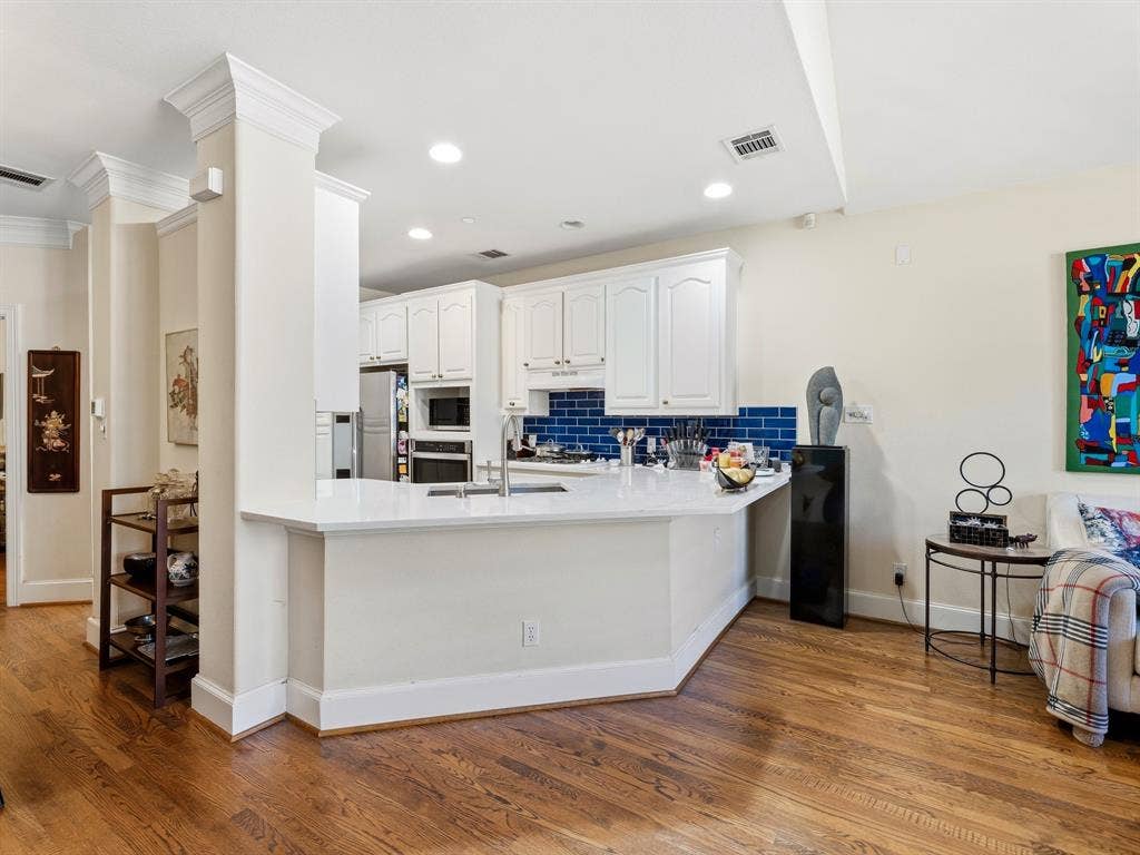 14567 Juliard Lane, Addison, TX 75001 Kitchen featuring white cabinetry, solid-surface countertops, blue subway tile backsplash, built-in stainless steel appliances, and wood-finish flooring