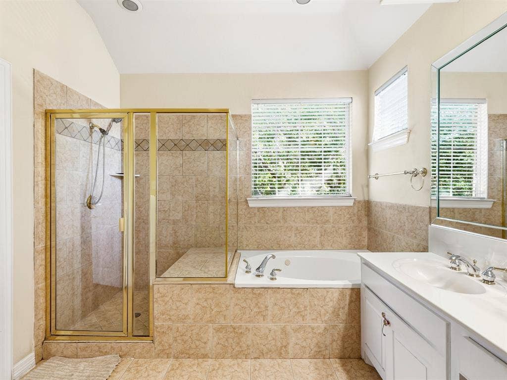 14567 Juliard Lane, Addison, TX 75001 Bathroom featuring a jetted tub, a glass-enclosed shower with tiled surround, white cabinetry, a dual-basin countertop, and a large wall-mounted mirror