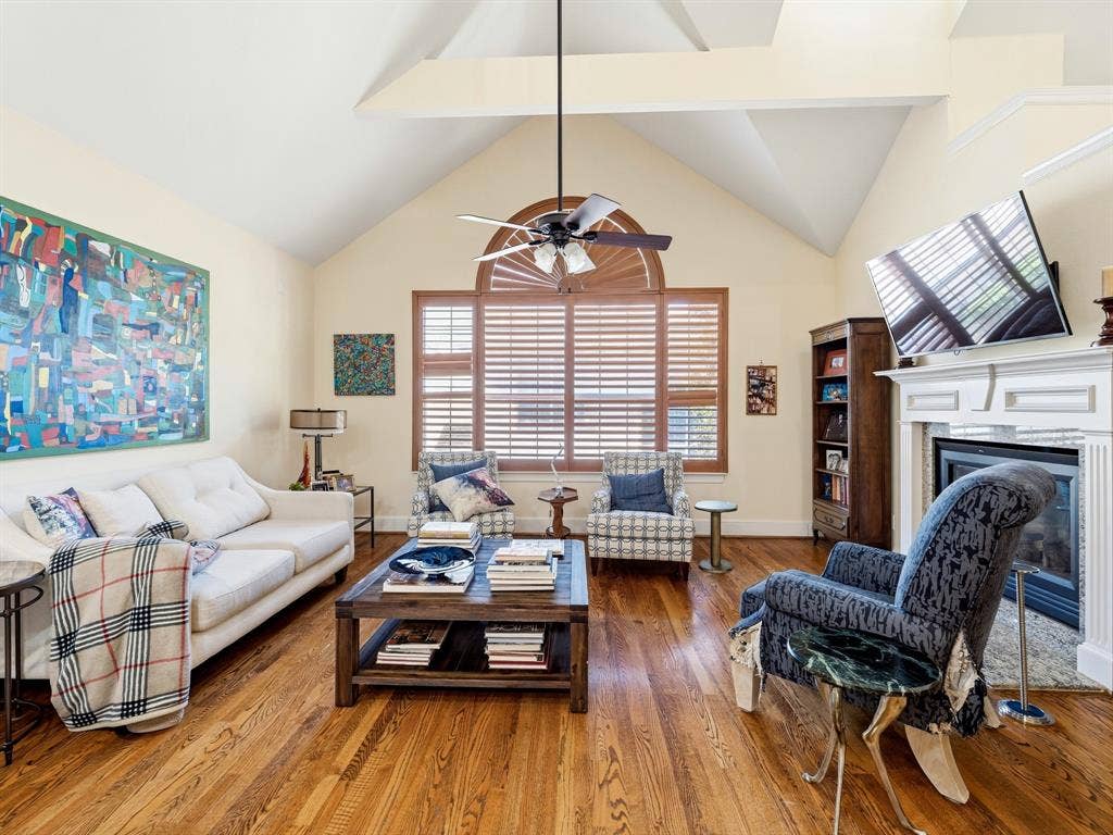 14567 Juliard Lane, Addison, TX 75001 Vaulted ceilings with wood-finish flooring, central ceiling fan, arched window, and a built-in fireplace featuring a decorative mantel