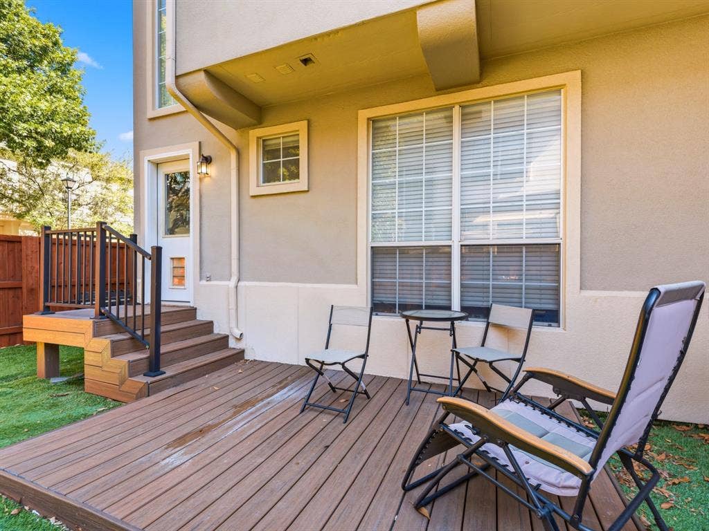 14567 Juliard Lane, Addison, TX 75001 Rear exterior featuring a multi-level wood-finish deck, metal railing, exterior wall-mounted light fixture, and a glass-panel door