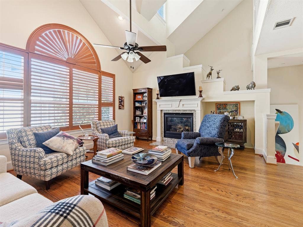14567 Juliard Lane, Addison, TX 75001 Vaulted ceilings featuring a large arched window with plantation shutters, wood-finish flooring, and a fireplace with a decorative mantle and tile surround