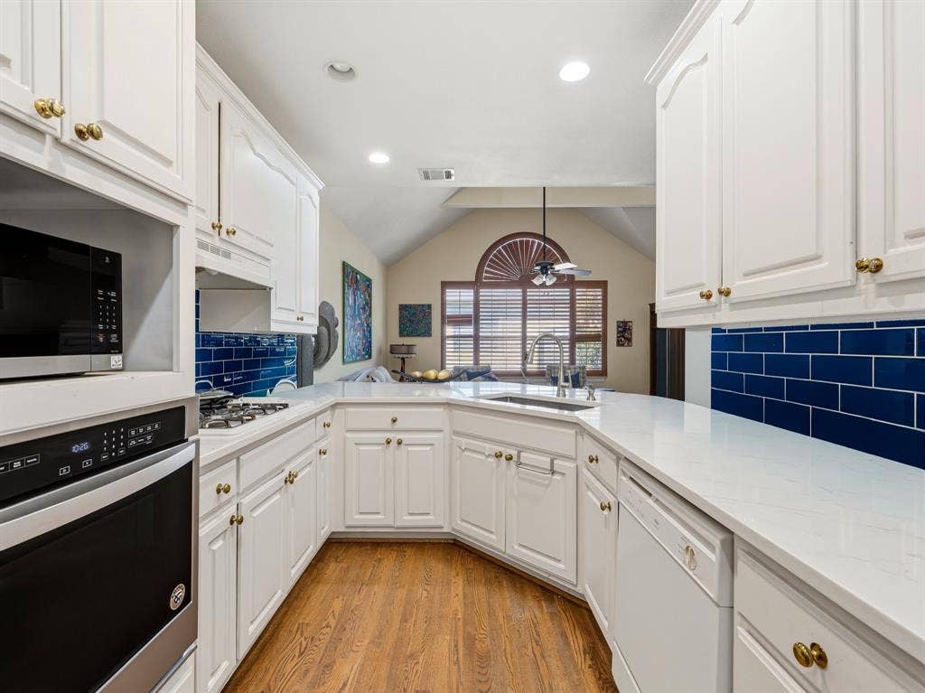 14567 Juliard Lane, Addison, TX 75001 Kitchen featuring white cabinetry, solid-surface countertops, blue subway tile backsplash, built-in stainless steel oven and microwave, and wood-finish flooring