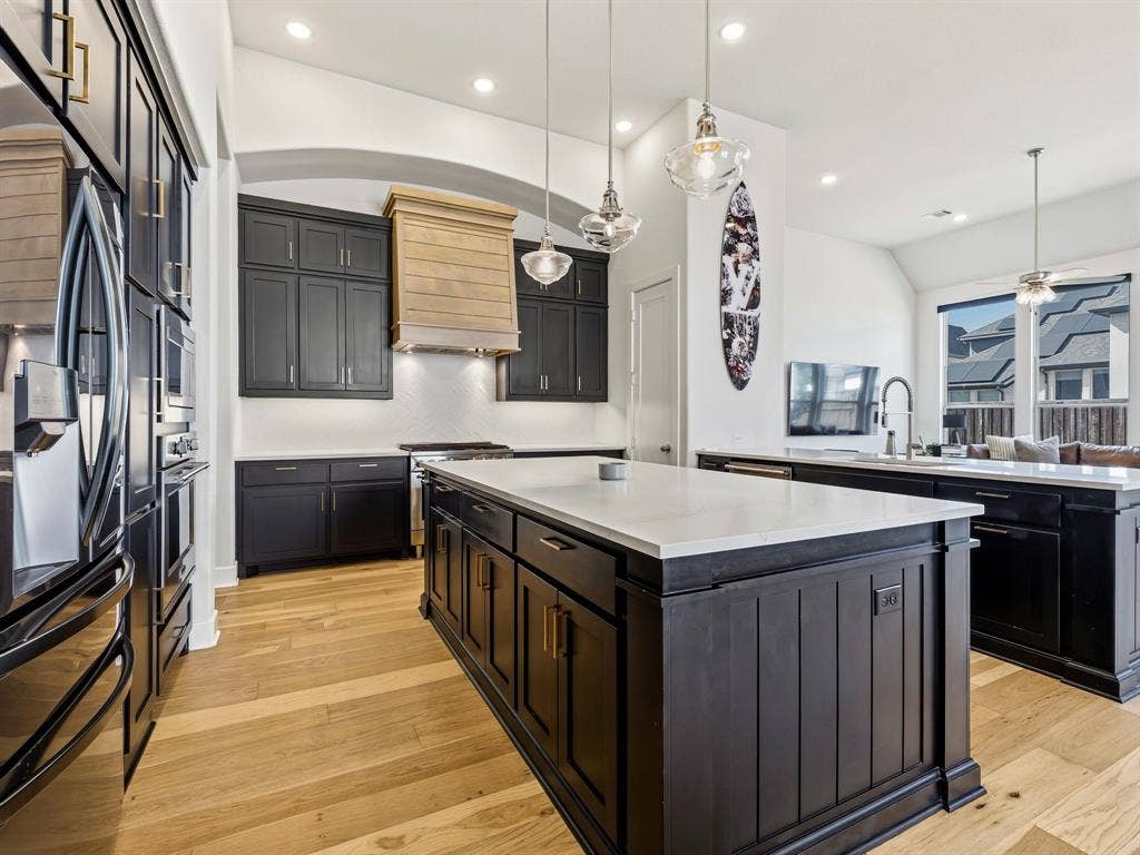 Kitchen featuring a central island with a solid surface countertop, custom dark cabinetry, wood-finish flooring, a wood-paneled range hood, and pendant lighting