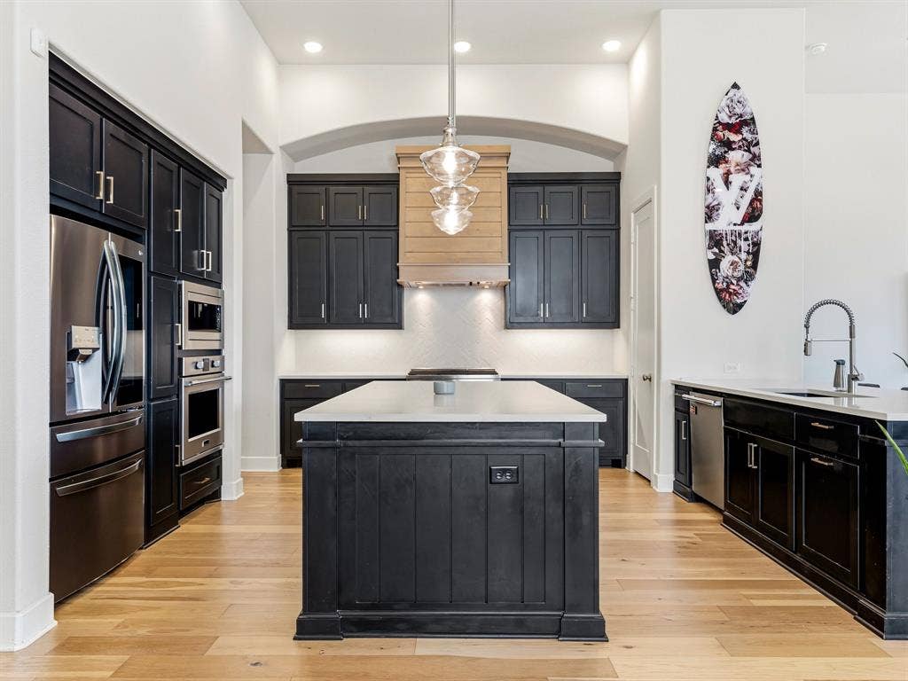 Kitchen featuring dark cabinetry, a central island with a light-toned countertop, wood-finish flooring, a wood-paneled range hood, and recessed lighting