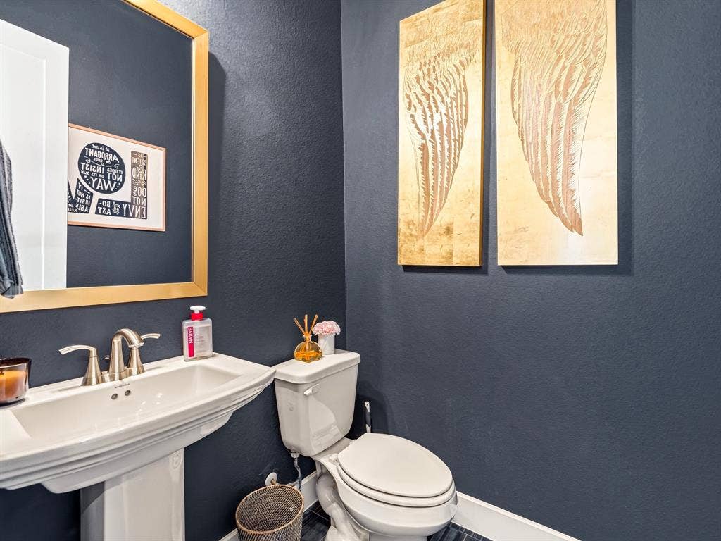 Pedestal sink with polished metal faucet hardware, large-scale gold-toned wall mirror, and dark-toned wall finish