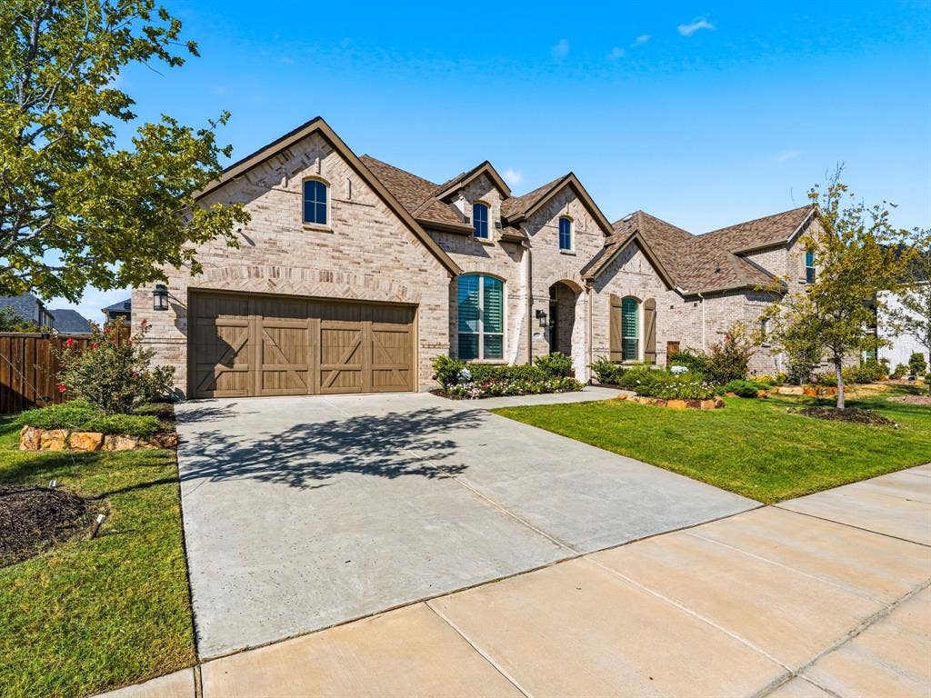 Brick exterior residence featuring a multi-gabled roofline, arched window detailing, wood-finish carriage-style garage doors, and manicured landscaping