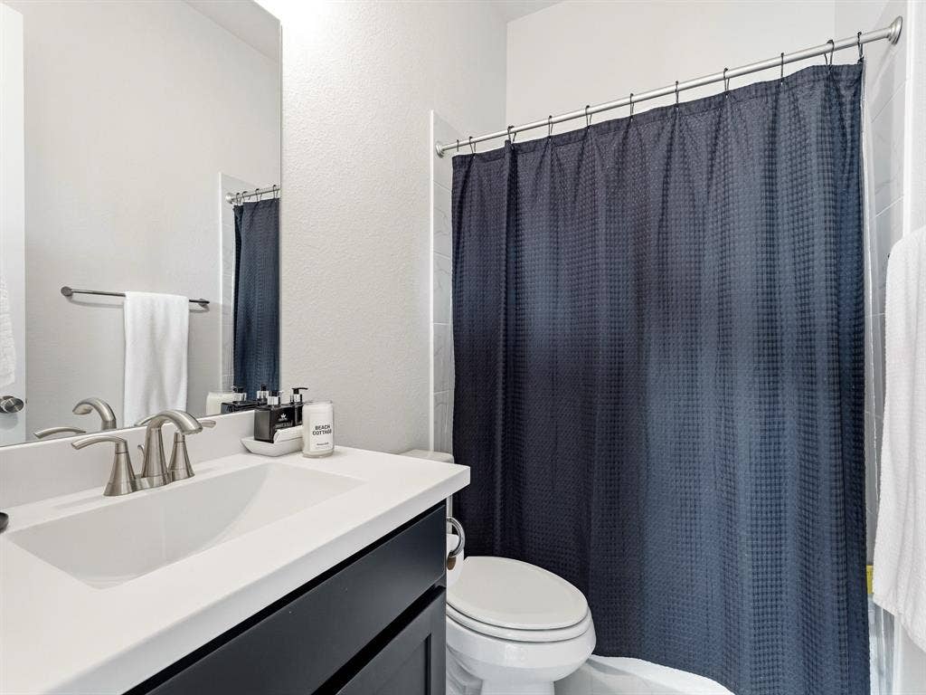 Bathroom featuring a dark wood-finish vanity, white countertop with an integrated basin, brushed nickel faucet, large wall mirror, and a tub-shower combination with tiled surround