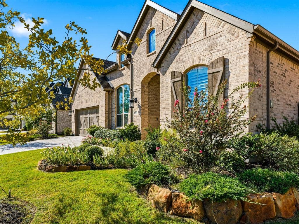 Brick exterior facade with arched window detailing, wood-finish shutters, multi-gable roofline, and stacked stone garden edging
