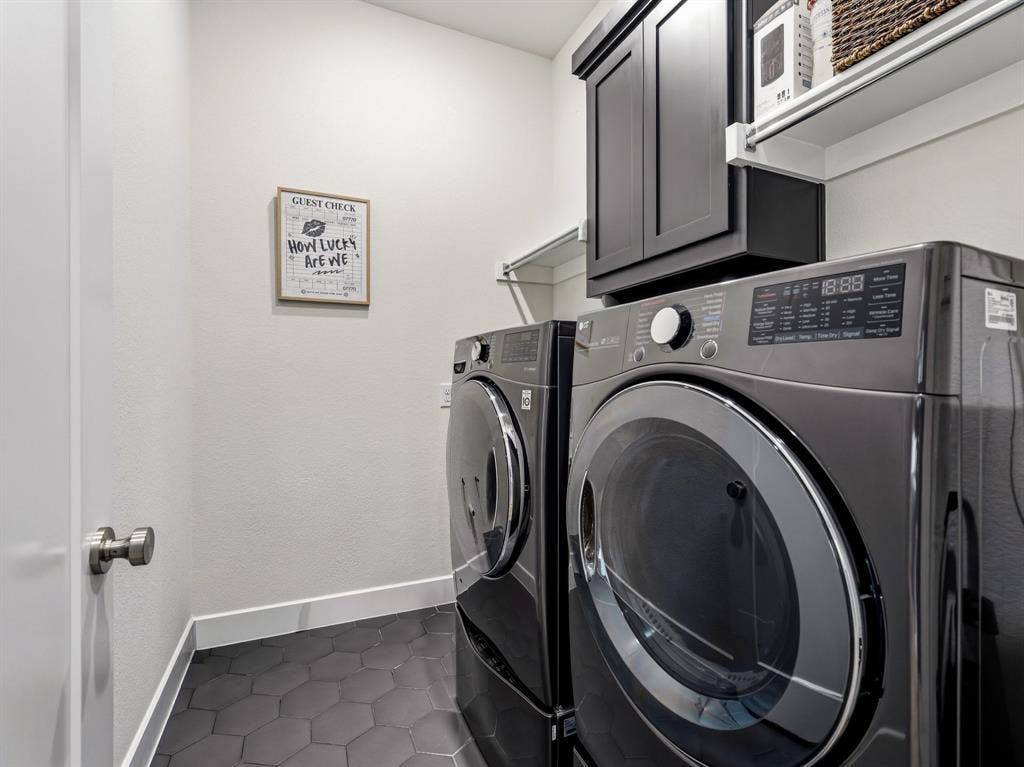 Laundry room featuring dark-finish wall-mounted cabinetry, white shelving, and charcoal hexagonal tile flooring