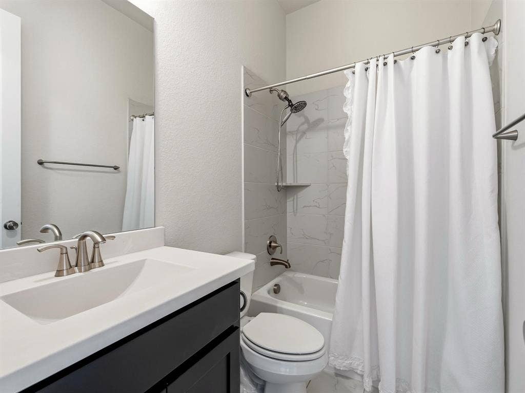 Bathroom featuring a white vanity with a solid surface countertop, an undermount sink with a brushed nickel faucet, a large wall-mounted mirror, and a tub with a tile surround