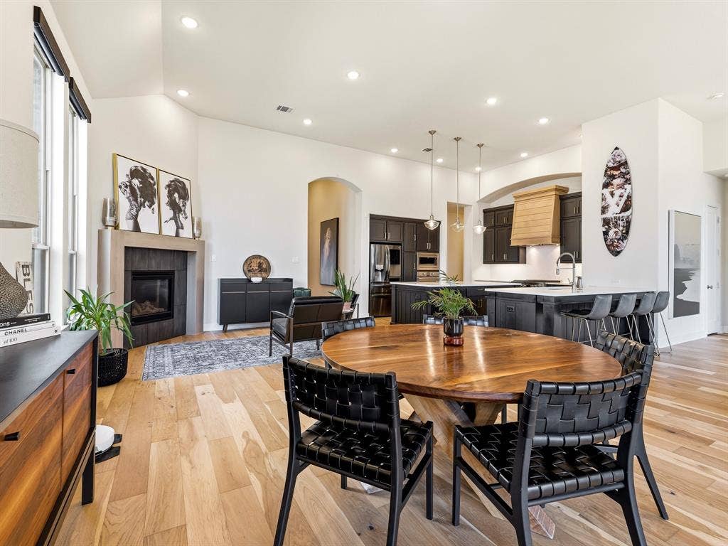 Open-concept interior featuring vaulted ceilings, wood-finish flooring, a stone-surround fireplace, dark cabinetry, and a large central kitchen island