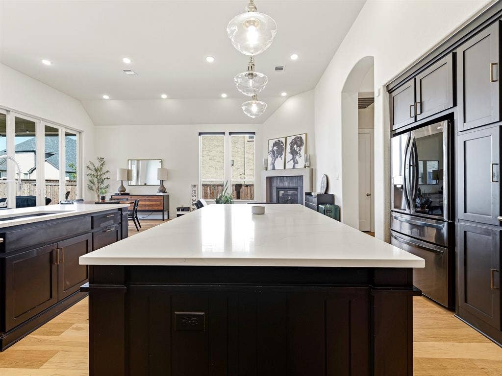 Kitchen featuring an expansive center island with a stone countertop, dark custom cabinetry, recessed lighting, glass pendant fixtures, and wood-finish flooring