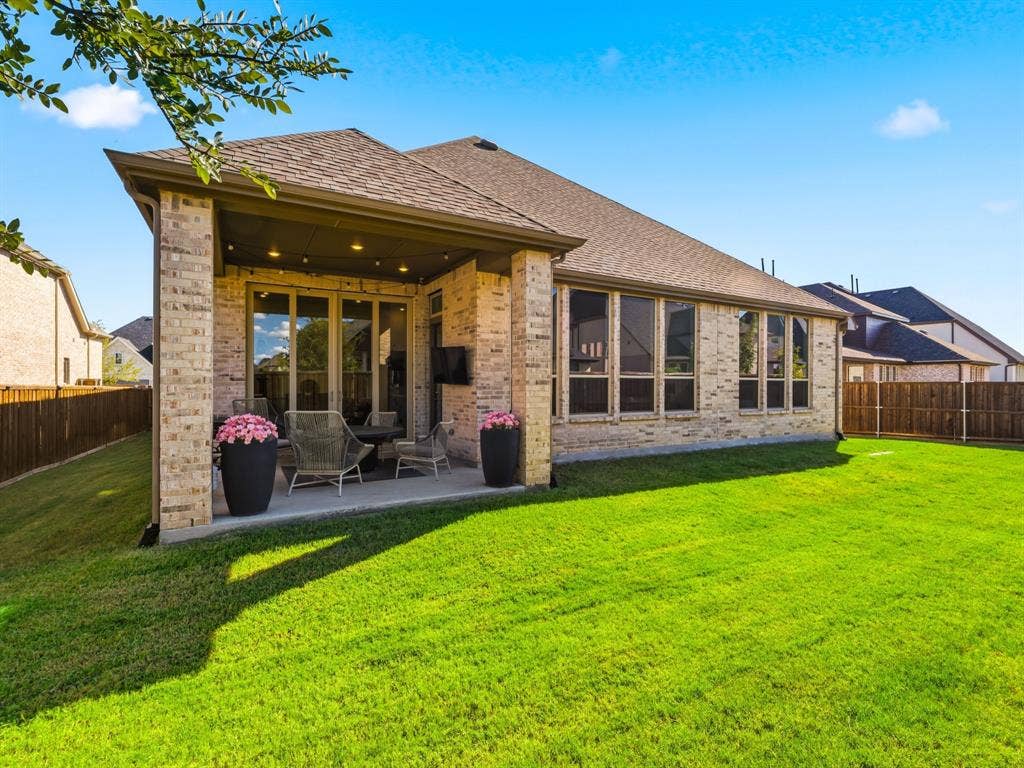 Brick exterior with covered concrete patio, recessed lighting, and expansive lawn enclosed by wood fencing