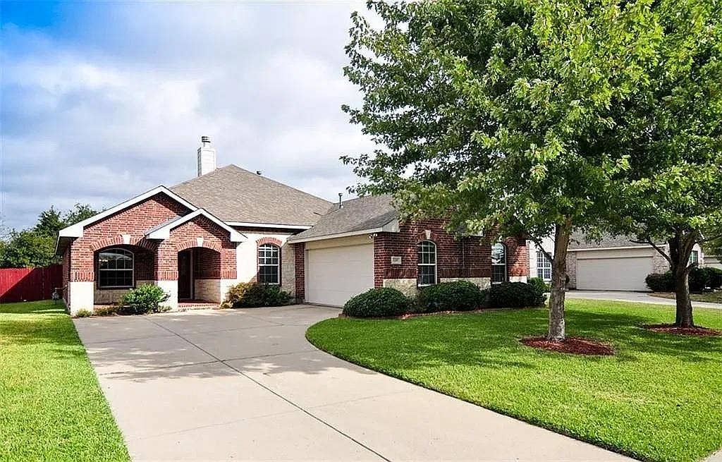 1207 Fox Trail Drive, Allen, TX 75002 Single-story brick exterior featuring a covered entryway, attached multi-car garage, arched window accents, and a concrete driveway
