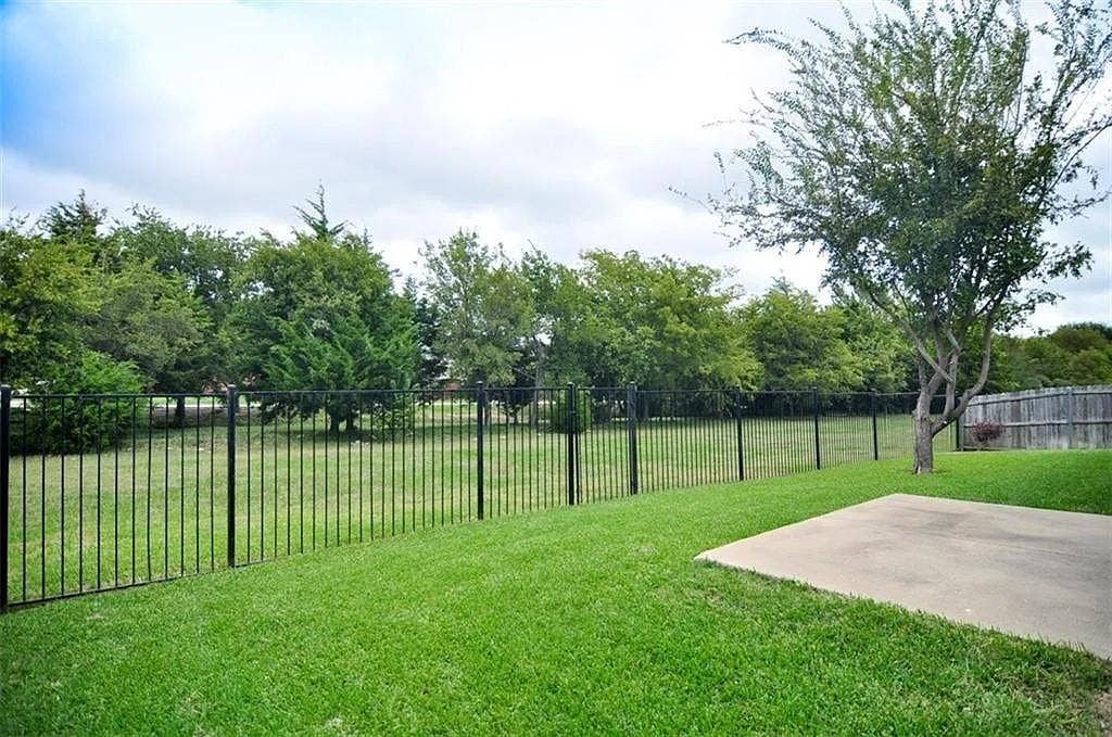 1207 Fox Trail Drive, Allen, TX 75002 Expansive backyard featuring a level lawn, concrete patio, black metal fencing, and mature trees