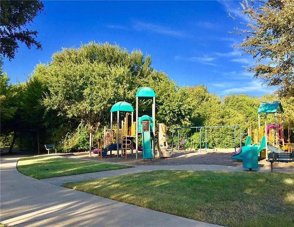1207 Fox Trail Drive, Allen, TX 75002 Outdoor recreation area featuring a multi-tiered playground structure, paved concrete walkways, benches, and manicured lawn surroundings
