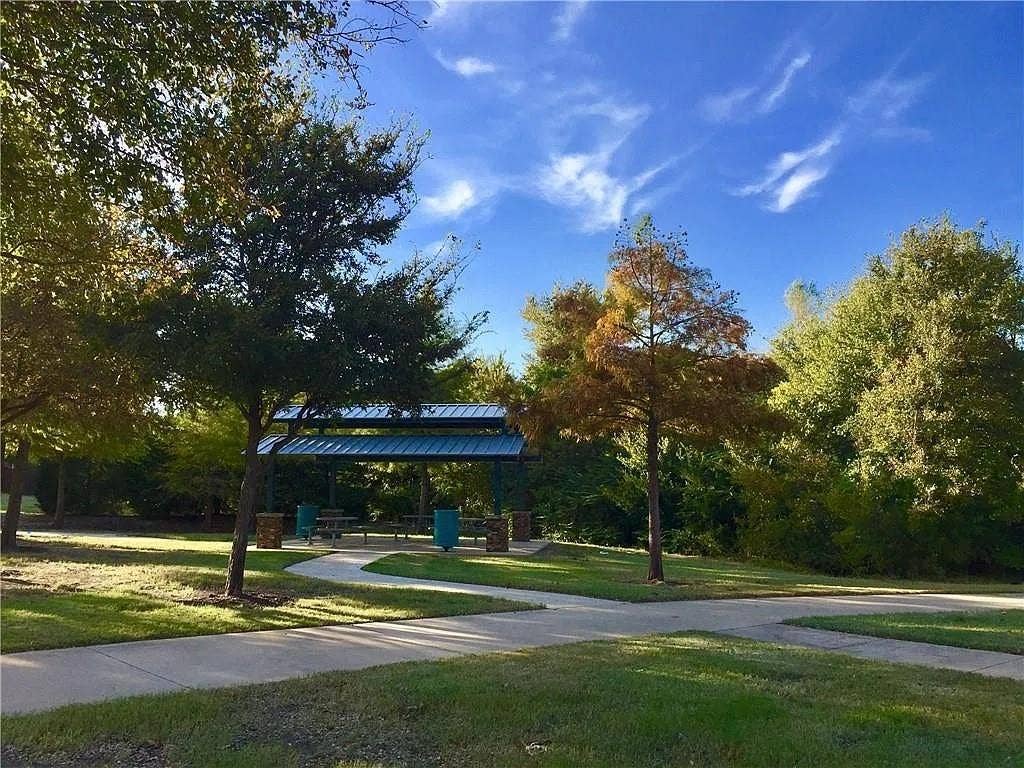 1207 Fox Trail Drive, Allen, TX 75002 Outdoor pavilion featuring a metal roof and stone-clad pillars, situated on a concrete walkway amidst mature trees and landscaped grounds