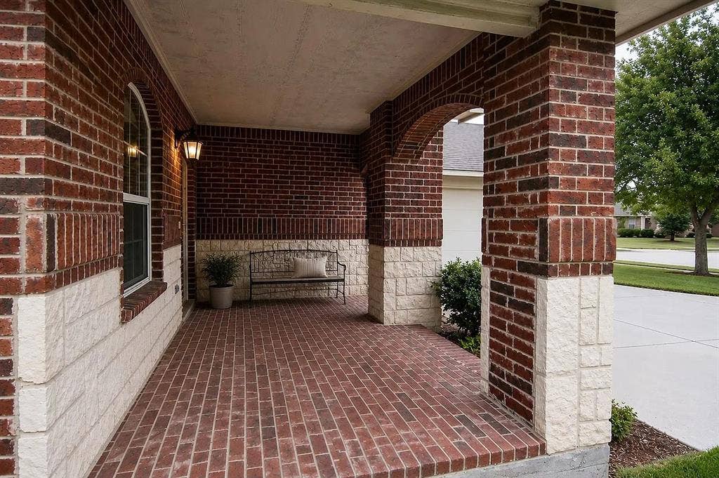 1207 Fox Trail Drive, Allen, TX 75002 Covered front porch featuring red brick flooring, arched architectural detailing, masonry columns, and a mixed brick and stone facade