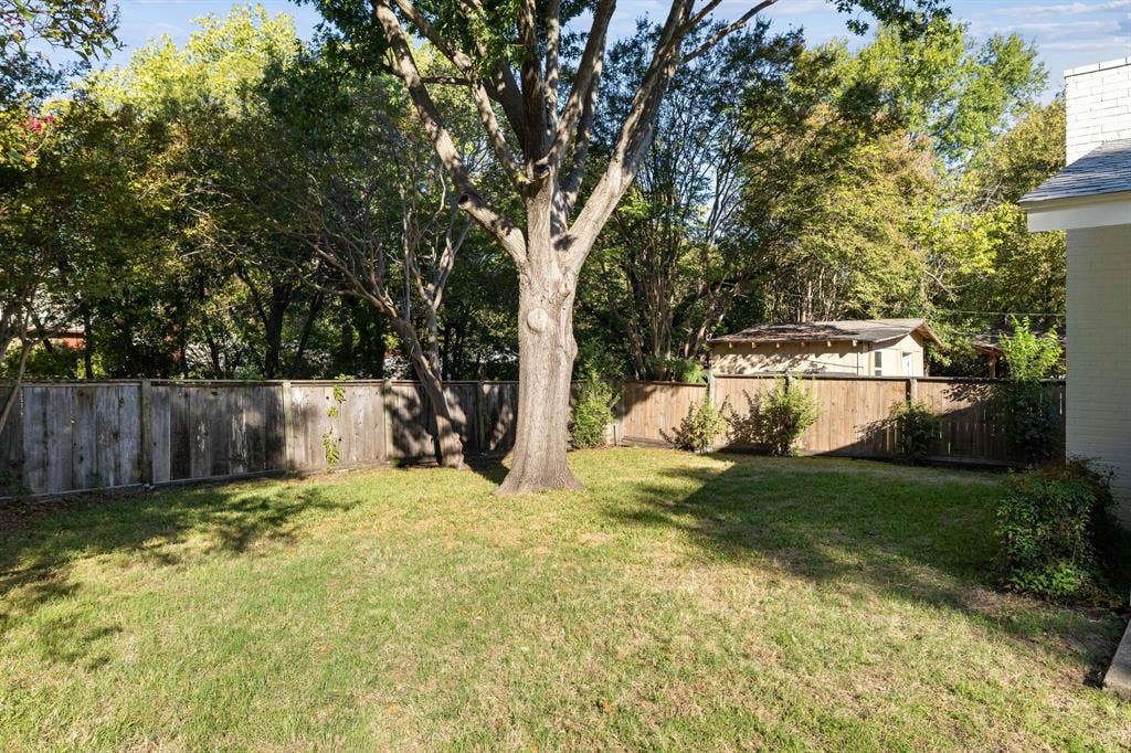 3209 Sheffield Street, Irving, TX 75062 Backyard featuring a manicured lawn, wood fencing, mature trees, and an accessory structure