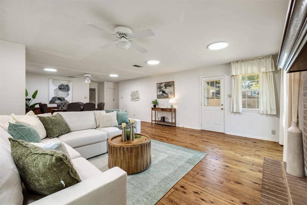 3209 Sheffield Street, Irving, TX 75062 Open-concept living space featuring wood-finish flooring, recessed lighting, white-painted brick fireplace surround, dual ceiling fans, and an exterior door with glass pane detail