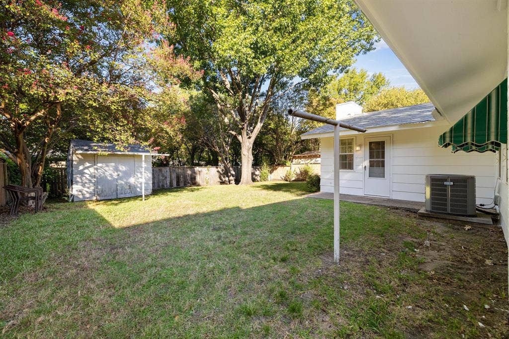 3209 Sheffield Street, Irving, TX 75062 Backyard featuring a manicured lawn, mature trees, exterior storage shed, and white horizontal siding