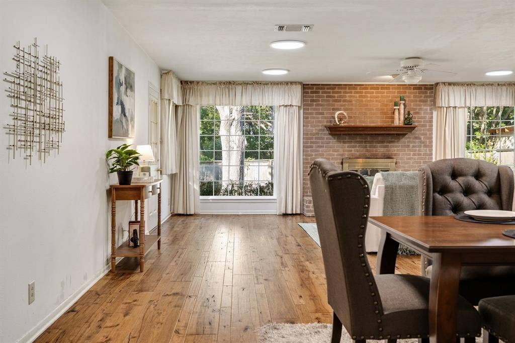 3209 Sheffield Street, Irving, TX 75062 Living space featuring wood-finish flooring, a floor-to-ceiling brick accent wall, a built-in wood mantel, and large windows with natural light