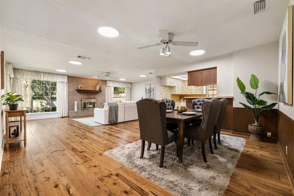 3209 Sheffield Street, Irving, TX 75062 Spacious room featuring wood-finish flooring, a brick fireplace with a wood mantel, ceiling-mounted light fixtures, and lower-wall wood paneling