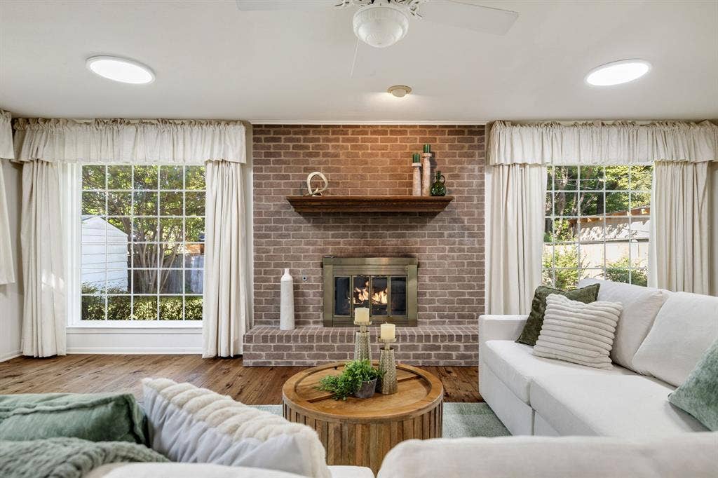 3209 Sheffield Street, Irving, TX 75062 Floor-to-ceiling brick fireplace surround with a wooden mantel and metal firebox, wood-finish flooring, and dual picture windows with grid muntins