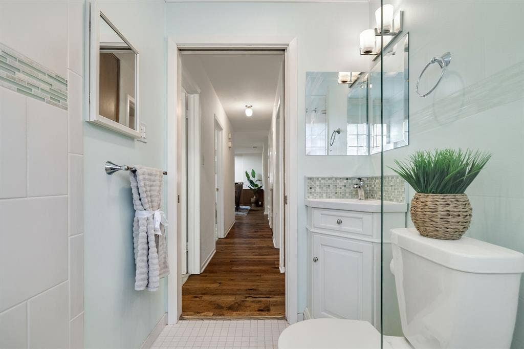 3209 Sheffield Street, Irving, TX 75062 Bathroom featuring a white corner vanity with a mosaic tile backsplash, a glass-enclosed shower, wall-mounted lighting, and wood-finish flooring