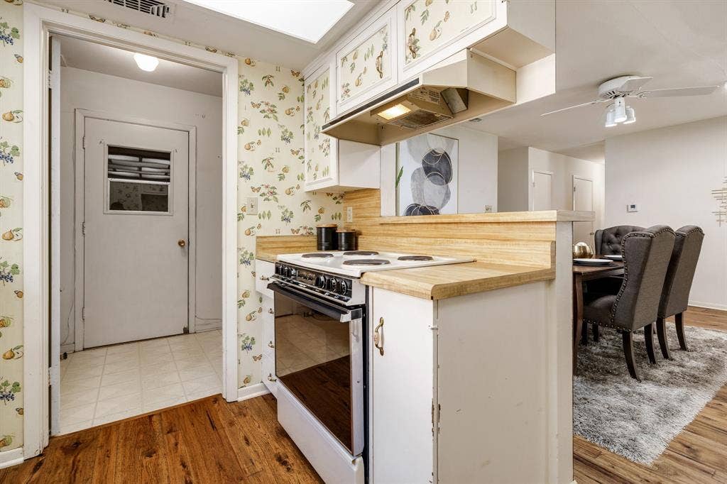 3209 Sheffield Street, Irving, TX 75062 Kitchen featuring wood-finish countertops, white cabinetry with patterned upper doors, a white electric range, and wood-finish flooring