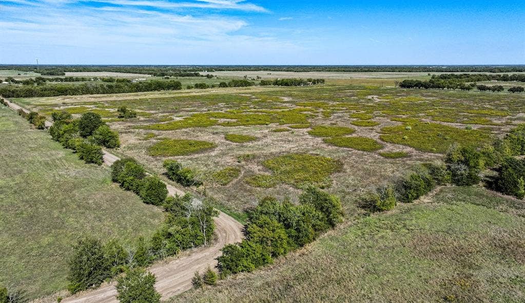 0 County Road 4604, Commerce, TX 75428 Expansive acreage featuring cleared meadows, clusters of mature trees, and an unpaved access road