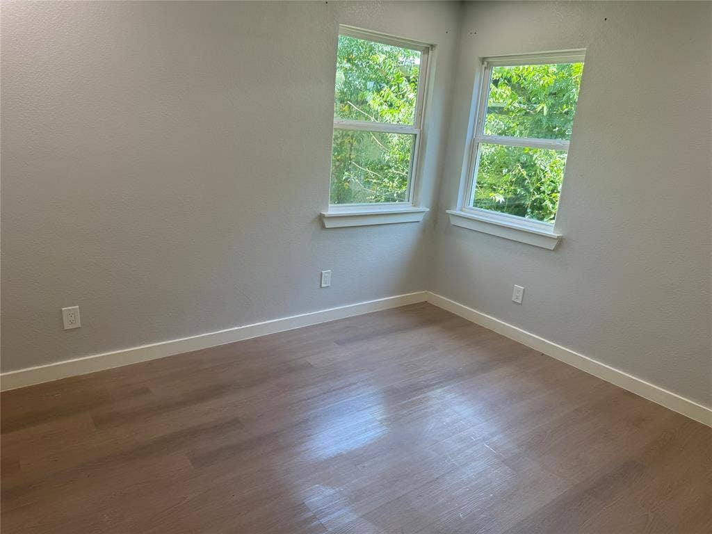 1123 Hansboro Avenue, Dallas, TX 75224 Room featuring neutral-toned walls, wood-finish flooring, and two windows with exterior natural greenery