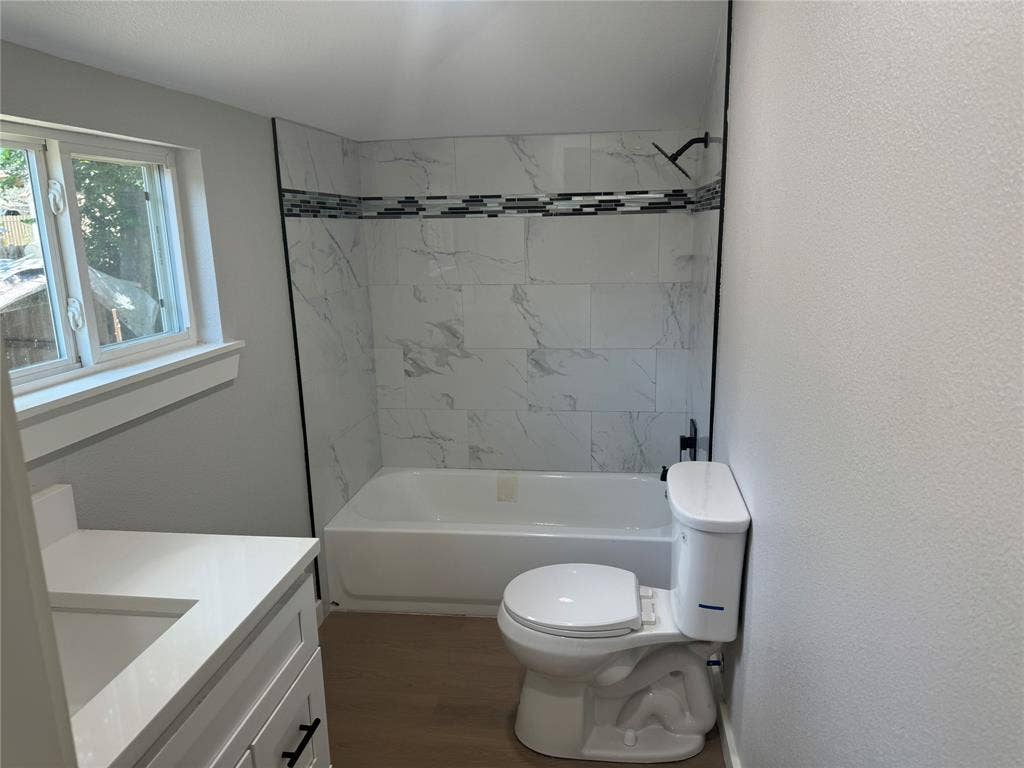 1123 Hansboro Avenue, Dallas, TX 75224 Bathroom featuring a white vanity with an integrated countertop, tub-shower combination with large-format wall tile, decorative mosaic tile inlay, and wood-finish flooring