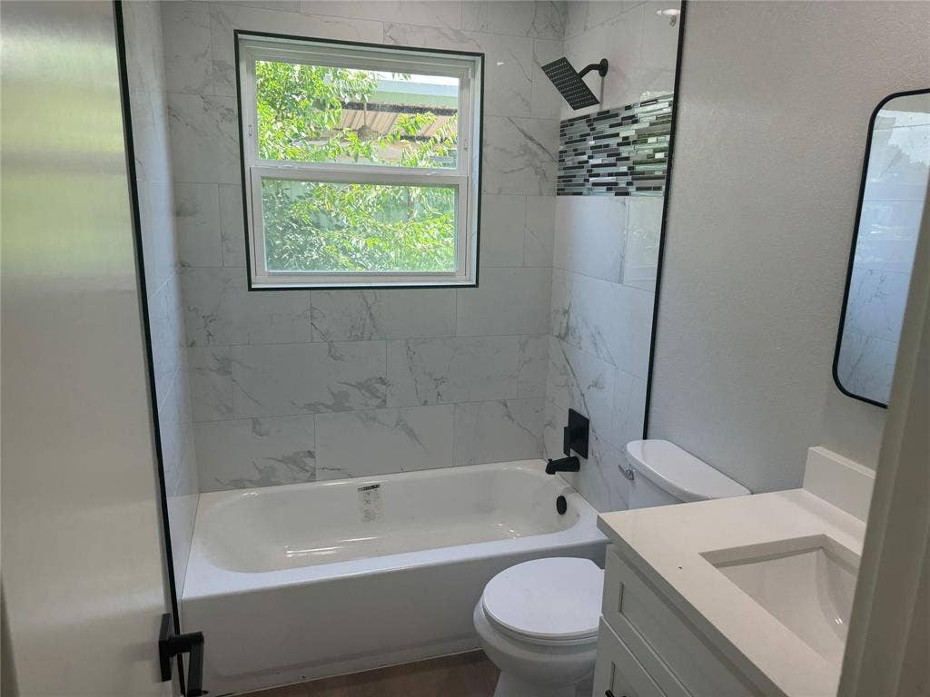 1123 Hansboro Avenue, Dallas, TX 75224 Bathroom featuring stone-finish wall tile, a built-in tub with matte black rain shower head and hardware, an integrated vanity, and a rectangular mirror
