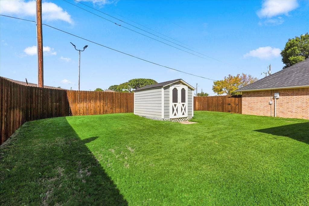 210 Santa Fe Trail, Waxahachie, TX 75165 Spacious backyard featuring a manicured lawn, full-perimeter wood fencing, and a detached storage structure