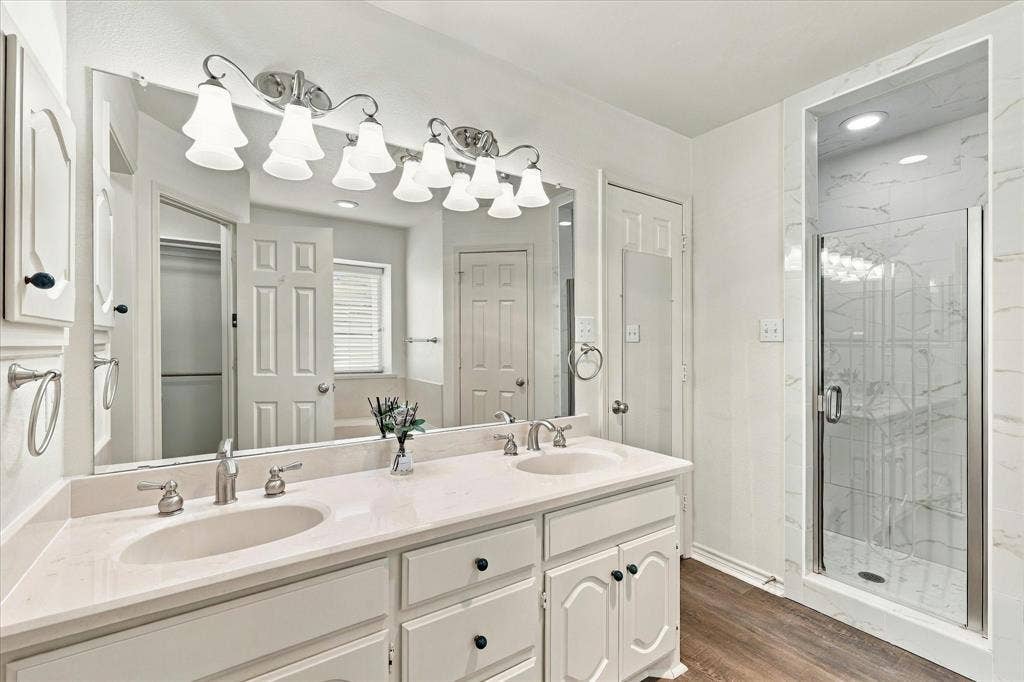 210 Santa Fe Trail, Waxahachie, TX 75165 Dual-sink vanity with a light-toned countertop, large-format mirror, overhead multi-light fixture, and walk-in shower with stone-finish tile surround and glass door