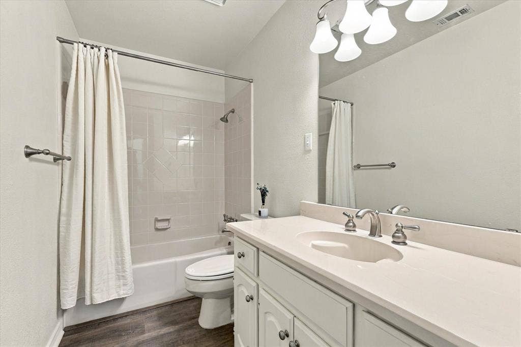 210 Santa Fe Trail, Waxahachie, TX 75165 Bathroom featuring a single-basin vanity with a solid-surface countertop, full-width wall mirror, wood-finish flooring, and a tiled shower-tub combination