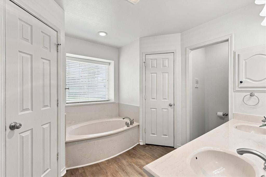 210 Santa Fe Trail, Waxahachie, TX 75165 Bathroom featuring a dual-sink vanity with a light-toned countertop, soaking tub with a deck surround, wood-finish flooring, and six-panel interior doors
