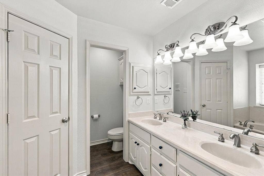 210 Santa Fe Trail, Waxahachie, TX 75165 Dual-sink vanity with a solid-surface countertop, white raised-panel cabinetry, full-width mirror, and five-light vanity fixture