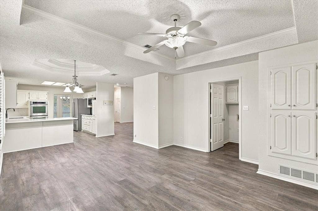210 Santa Fe Trail, Waxahachie, TX 75165 Interior area featuring wood-finish flooring, tray ceilings with crown molding, a central ceiling fan with integrated lighting, a built-in storage cabinet, and a kitchen equipped with a breakfast bar and stainless steel wall oven