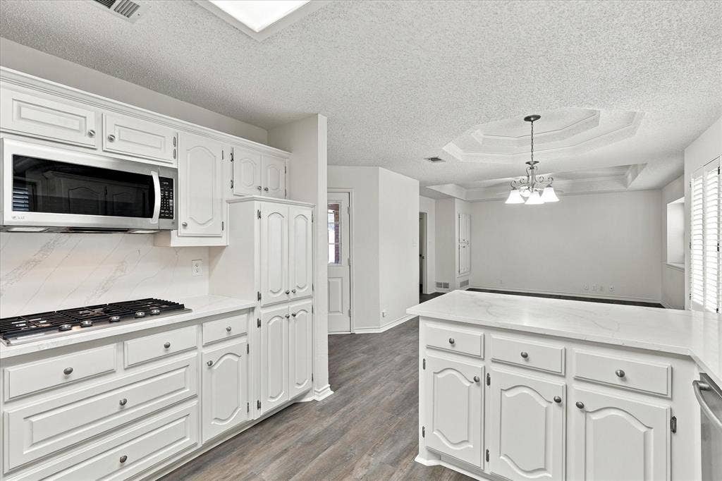 210 Santa Fe Trail, Waxahachie, TX 75165 Kitchen featuring white cabinetry, solid-surface countertops, integrated stainless steel microwave, gas cooktop, and wood-finish flooring