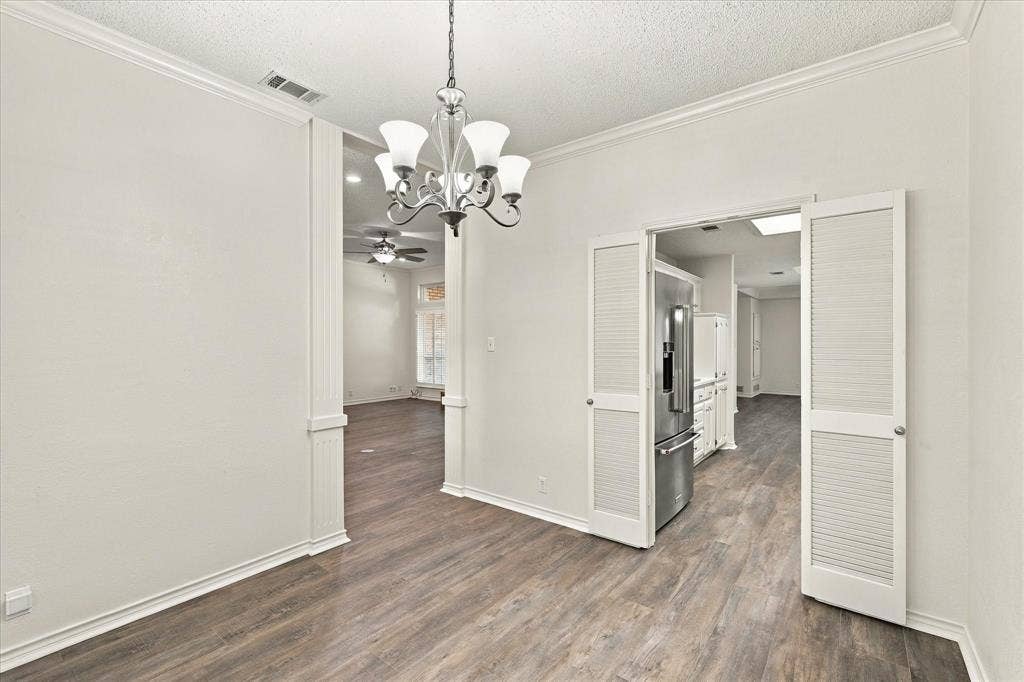 210 Santa Fe Trail, Waxahachie, TX 75165 Interior space featuring wood-finish flooring, crown molding, and a tiered chandelier with glass shades, complemented by white louvered double doors