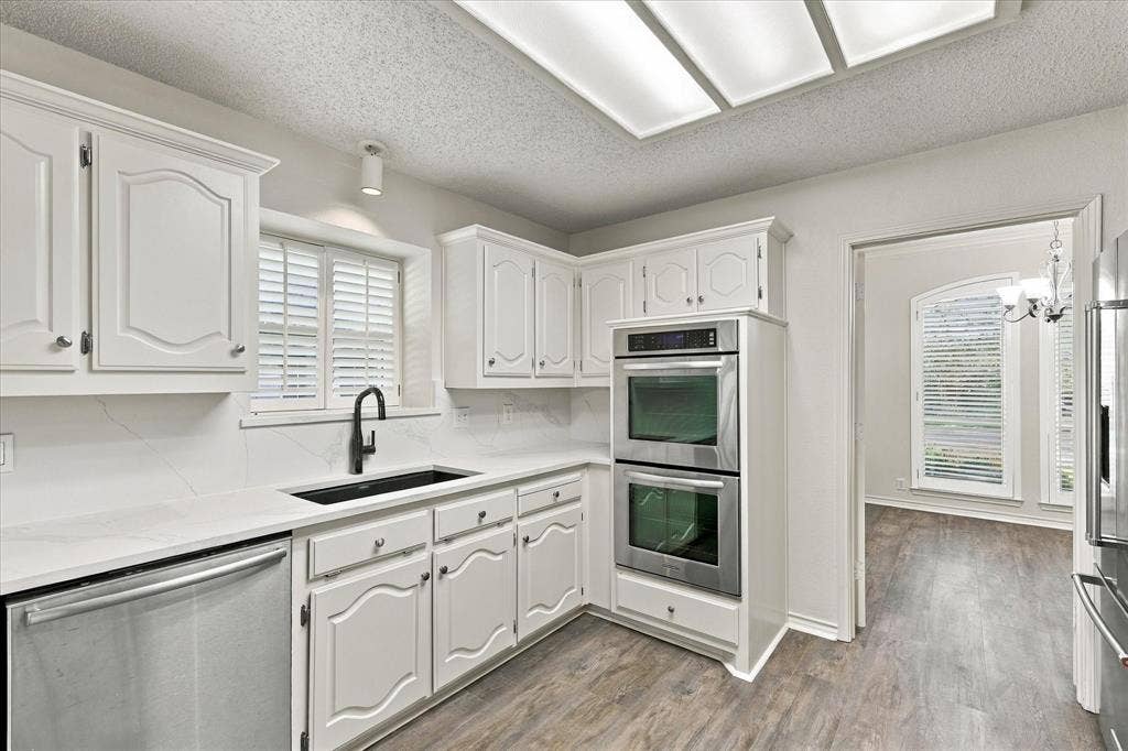 210 Santa Fe Trail, Waxahachie, TX 75165 Kitchen featuring white cabinetry with raised-panel detailing, light-toned stone-finish countertops, stainless steel double wall ovens, a matte black faucet with an undermount sink, and recessed panel lighting