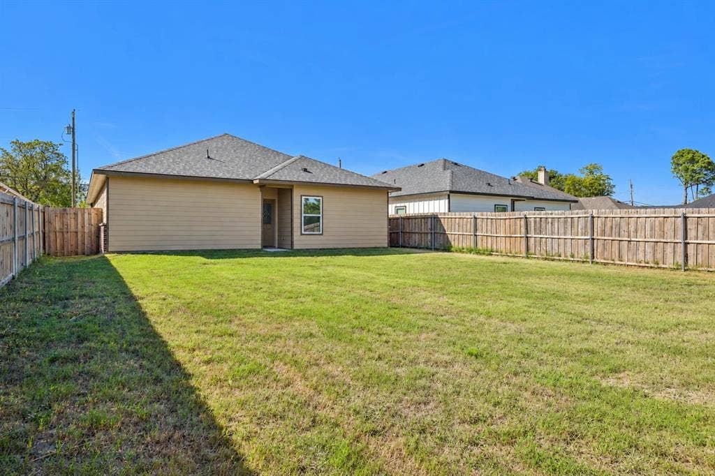 1221 S Rockwall Avenue, Terrell, TX 75160 Expansive backyard featuring a level lawn, full wood-plank privacy fencing, and a neutral-toned exterior with a shingled hip roof