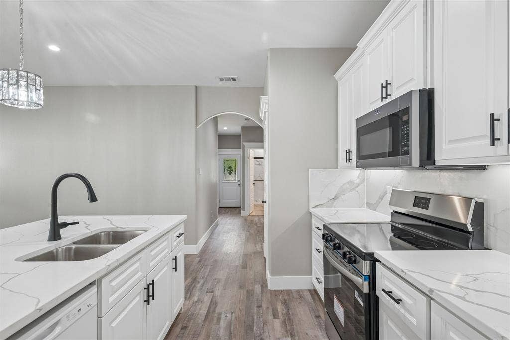 1221 S Rockwall Avenue, Terrell, TX 75160 Kitchen featuring white shaker-style cabinetry, white countertops with grey veining, a stainless steel microwave and range, and wood-finish flooring
