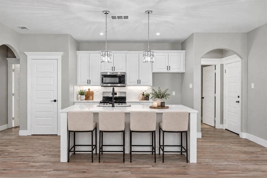 1221 S Rockwall Avenue, Terrell, TX 75160 Kitchen featuring white cabinetry, an oversized quartz-topped island, wood-finish flooring, stainless steel appliances, and dual pendant lighting